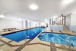 A large indoor swimming pool with clear blue water, surrounded by tiled flooring and white walls.