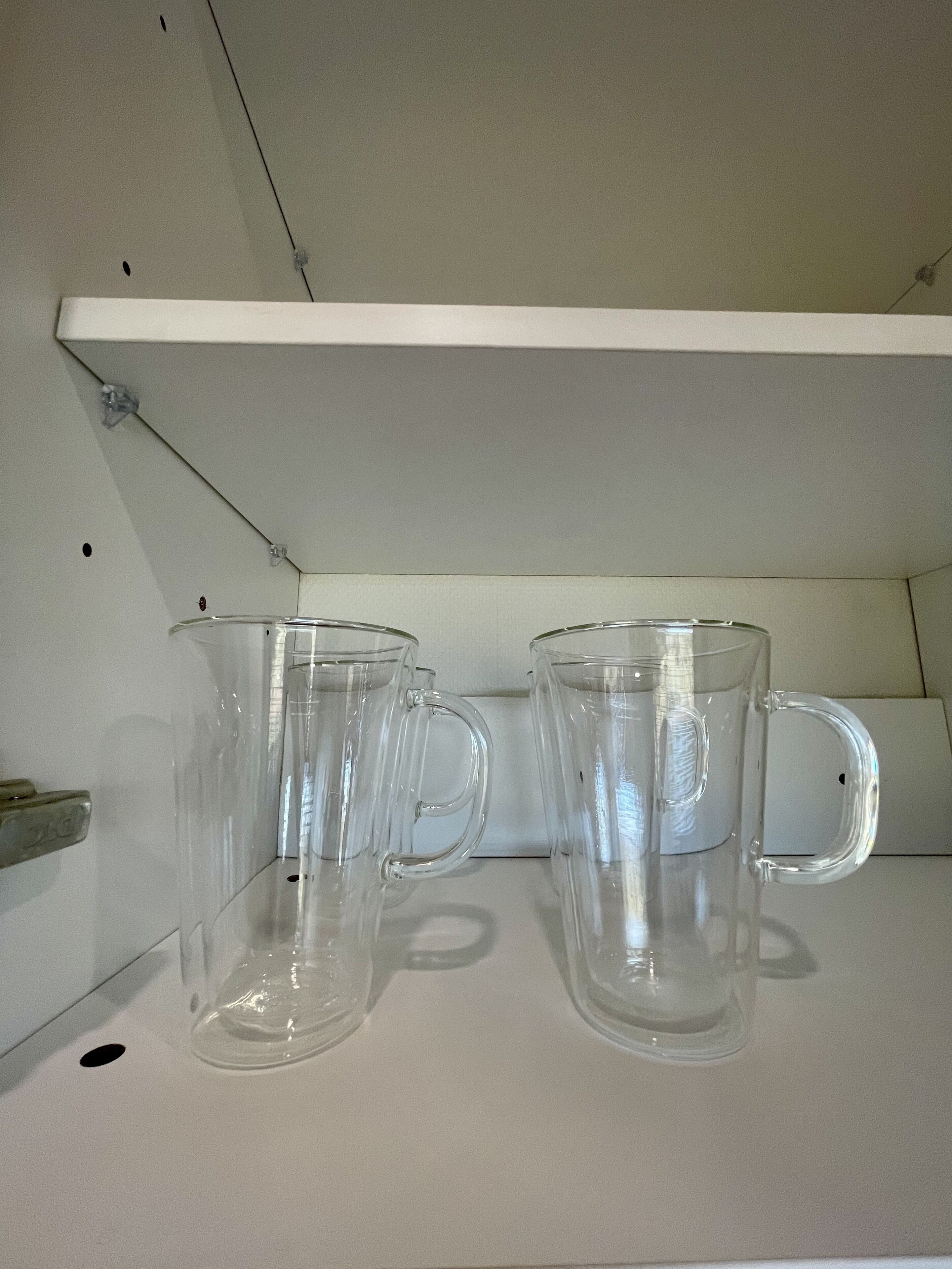 Two clear glass mugs on a white shelf.