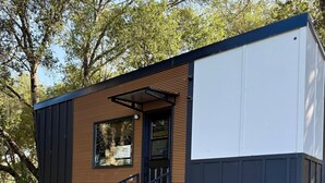 A modern cabin with a wooden exterior, a stone patio, and a view of the surrounding trees. - A Vineyard TinyHome Escape (Angels Camp)