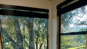 A bedroom with a large bed, a wooden headboard, and a view of a forest through large windows. - A Vineyard TinyHome Escape (Angels Camp)