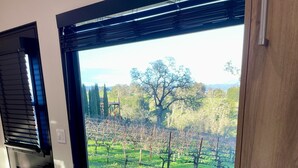 A room with a wooden table and chairs, a window with a view of a vineyard, and a wooden cabinet. - A Vineyard TinyHome Escape (Angels Camp)