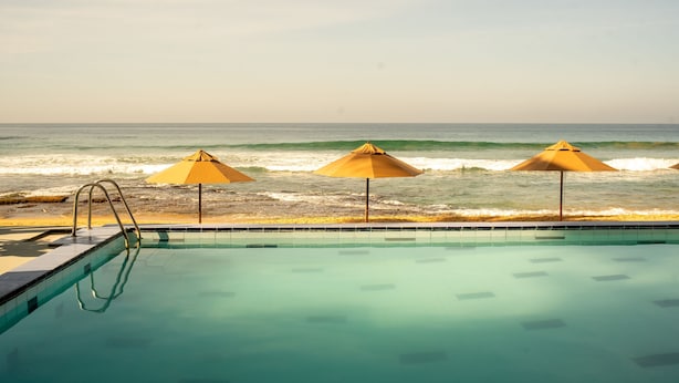 Una piscina amb tres ombrelles i vista a l'oceà.