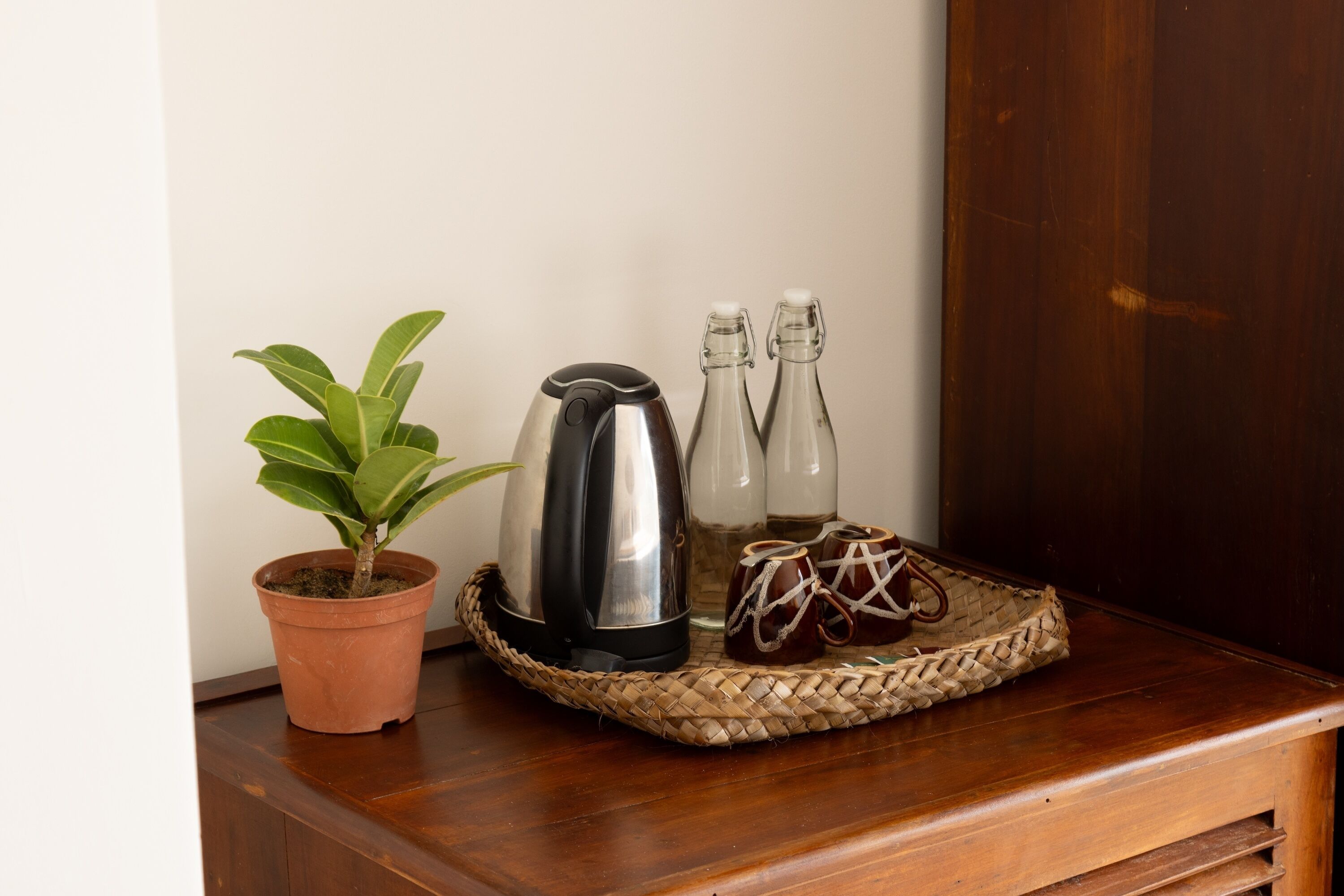 Een houten tafel met een plant in pot, een koffiezetapparaat, twee flessen en twee keramische kopjes.