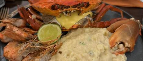 A seafood platter with a crab, shrimp, and a mound of mashed potatoes, served on a dark plate.