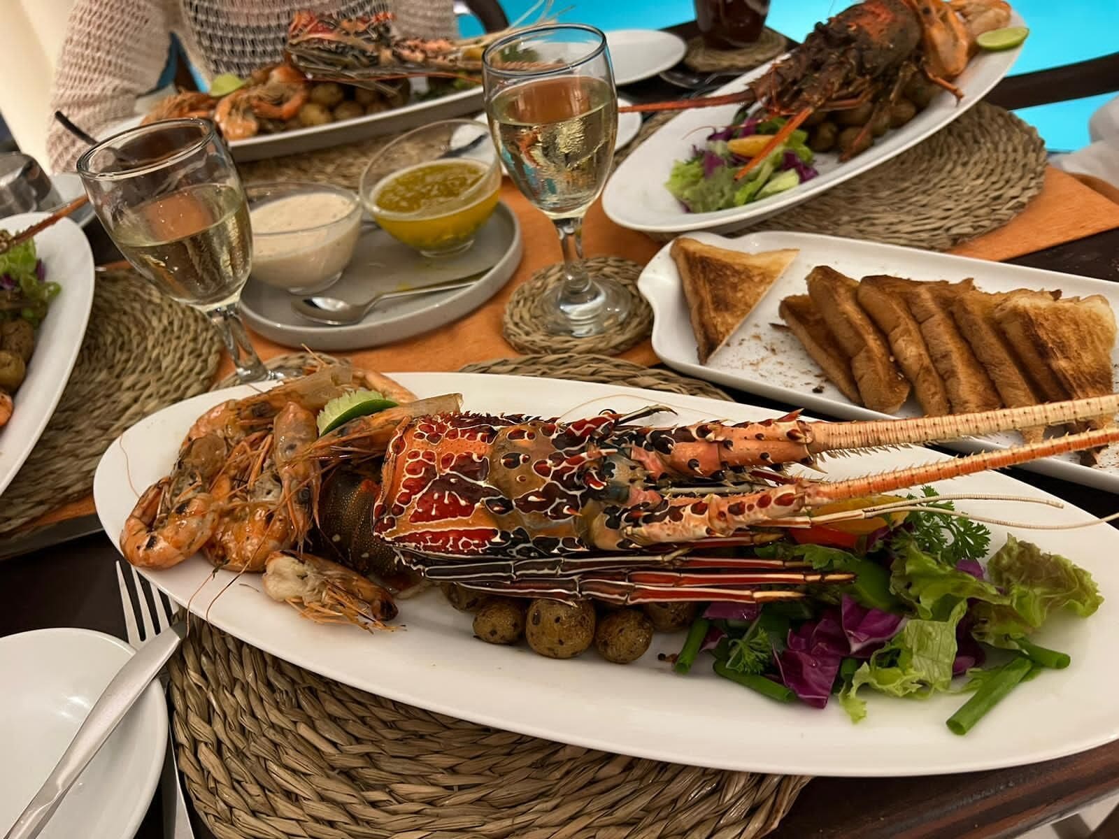 A seafood platter with a lobster, shrimp, and salad, accompanied by drinks and bread.