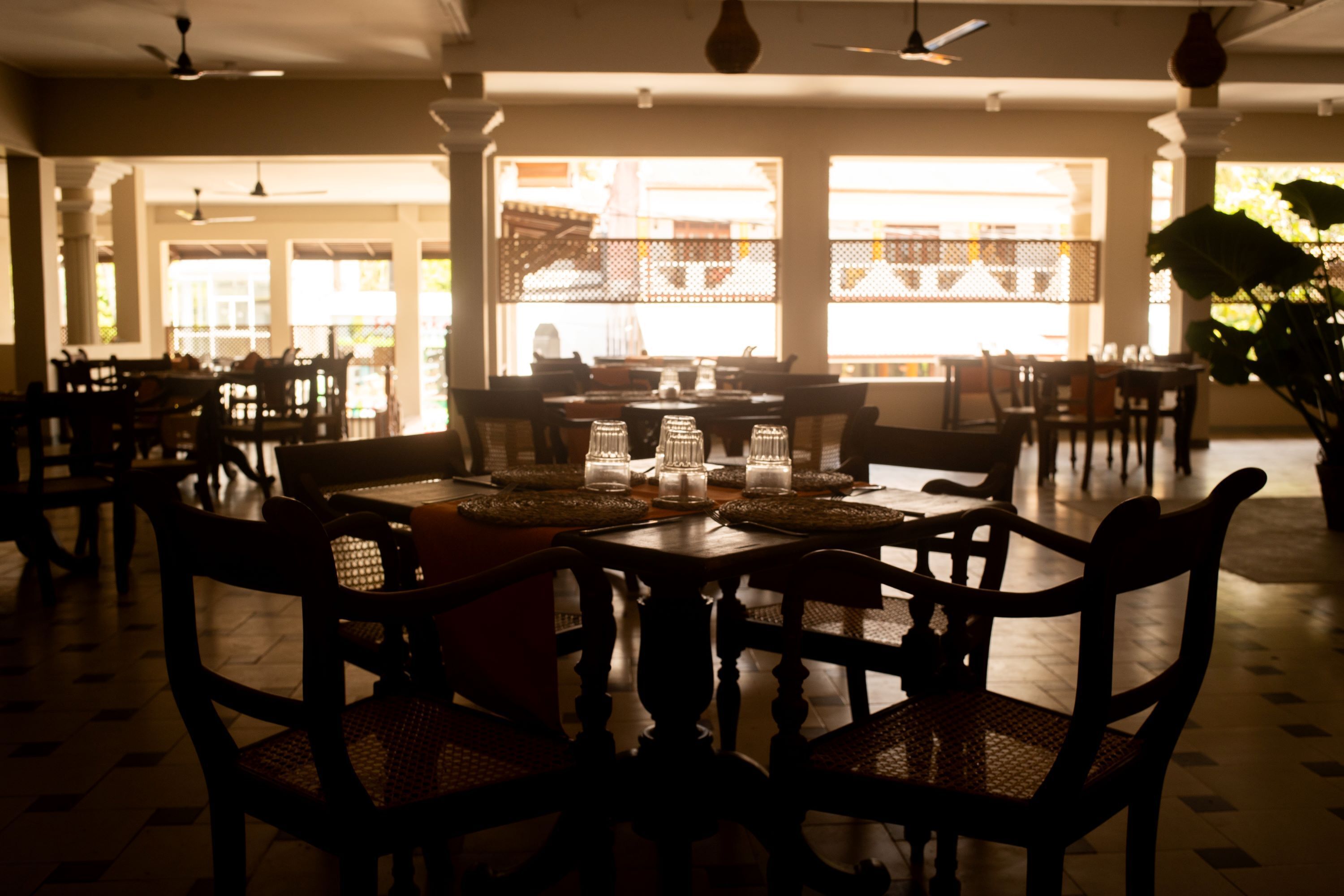 A spacious dining area with wooden tables and chairs, large windows allowing natural light, and a view of the street outside.
