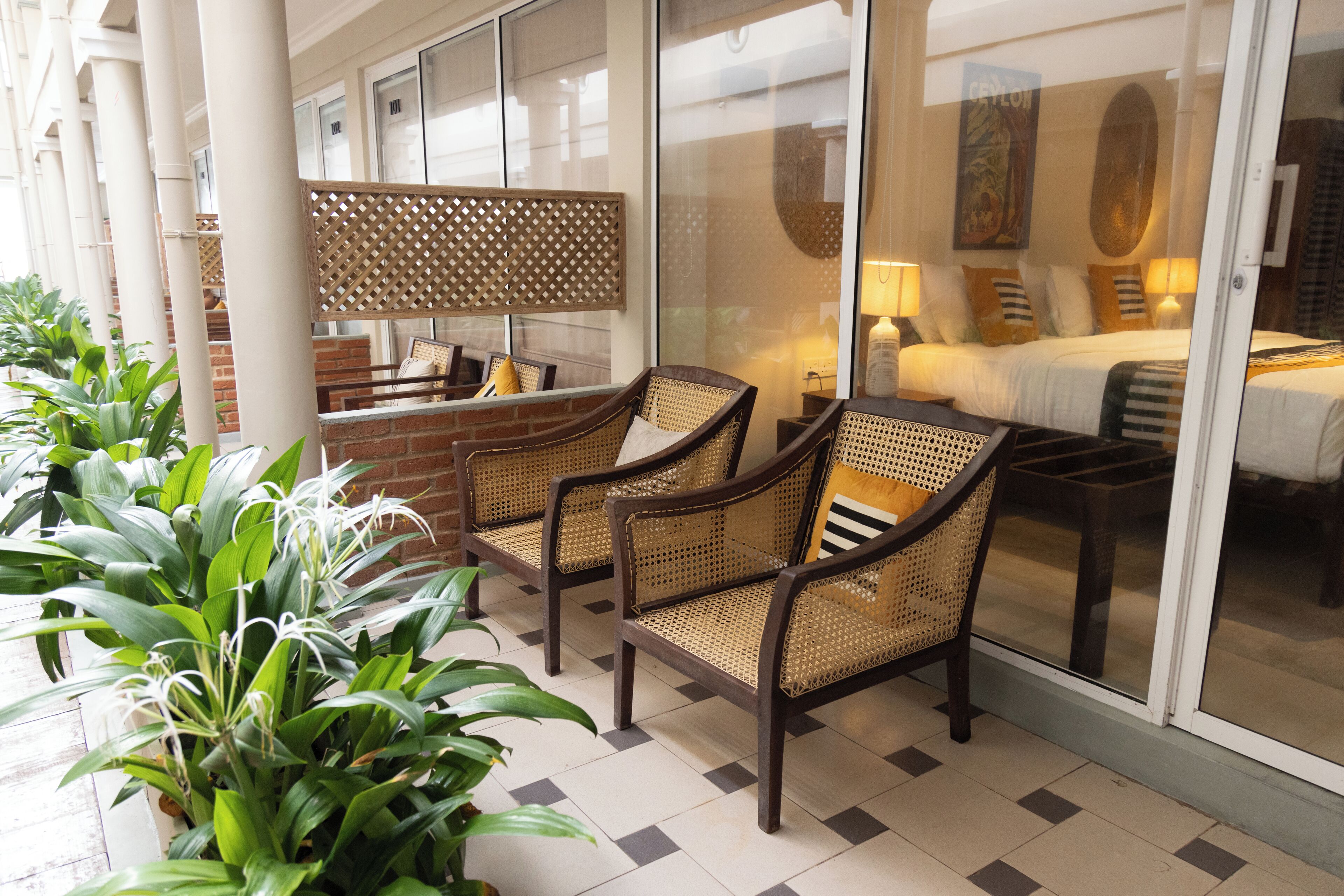 A hotel lobby with wicker chairs, a brick wall, and a glass door leading to a bedroom.