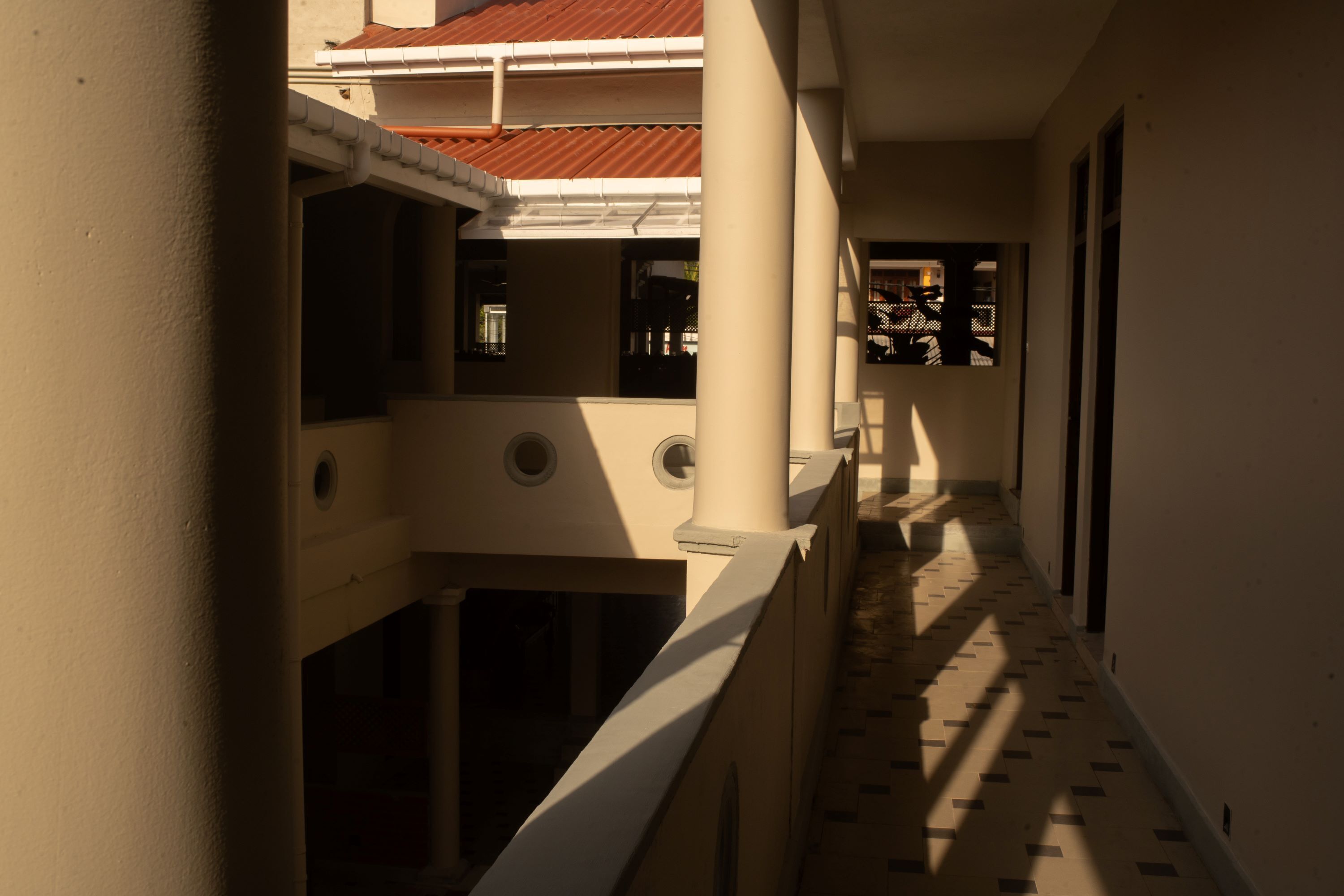 A corridor with a tiled floor, white walls, and a red-tiled roof.
