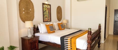 A bedroom with a wooden bed, white bedding, and decorative pillows. There is a nightstand with a lamp and a potted plant.