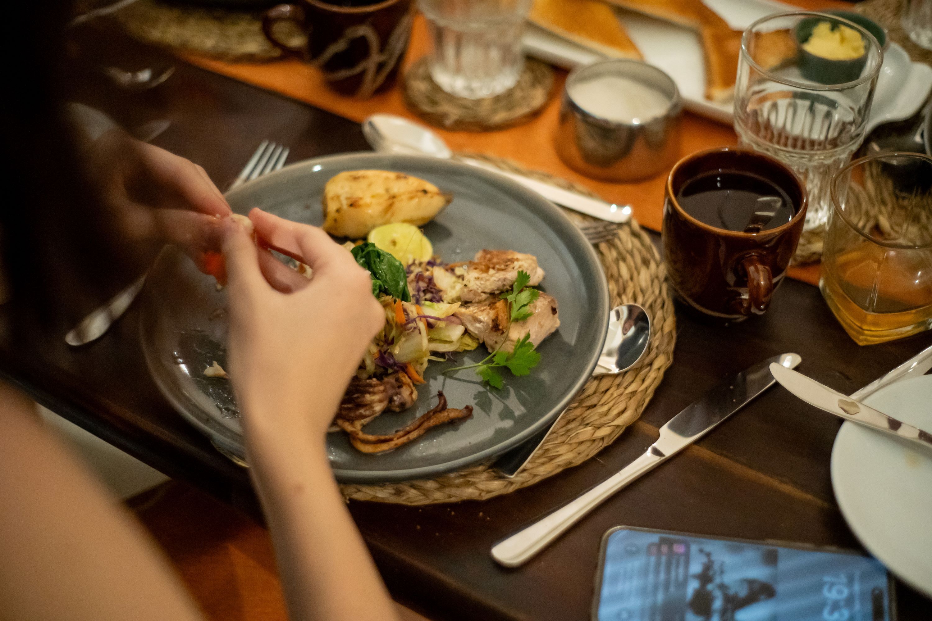 A dining table with a plate of food, cutlery, and a smartphone.
