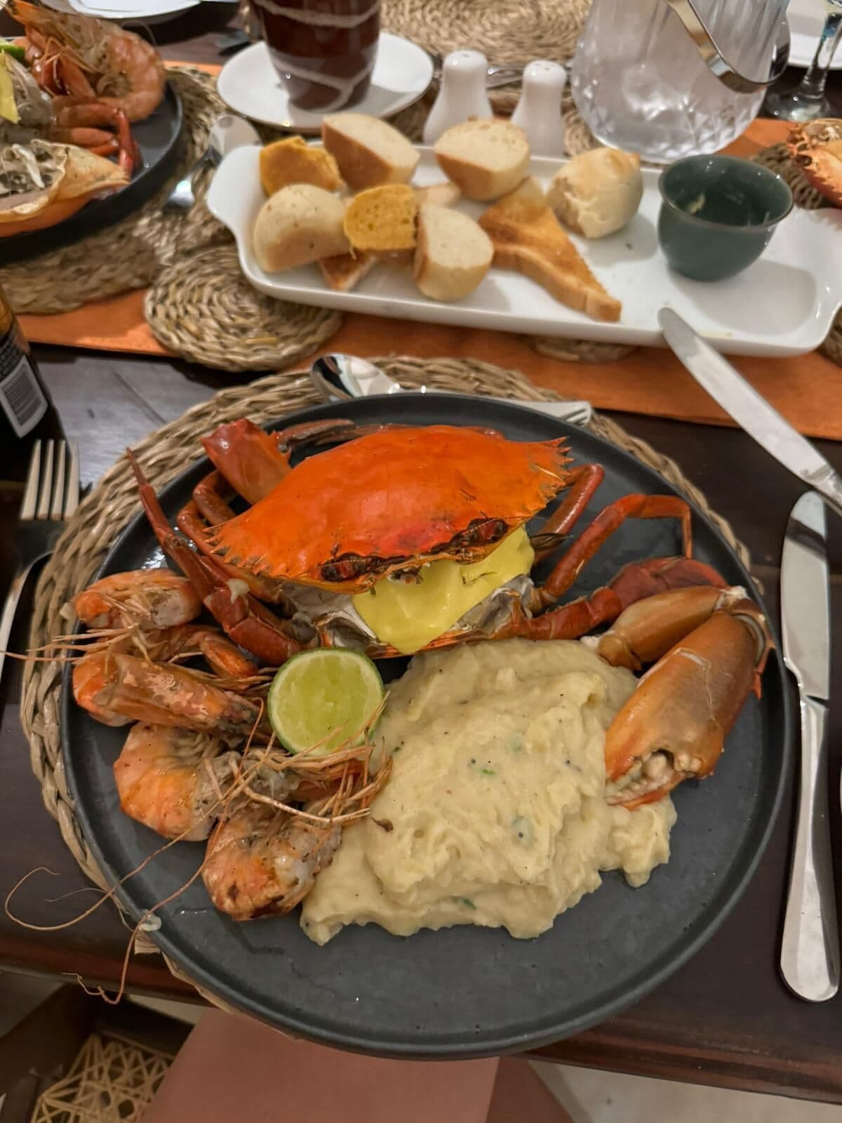A seafood platter with crab legs, shrimp, and a side of mashed potatoes, accompanied by bread and a green sauce.