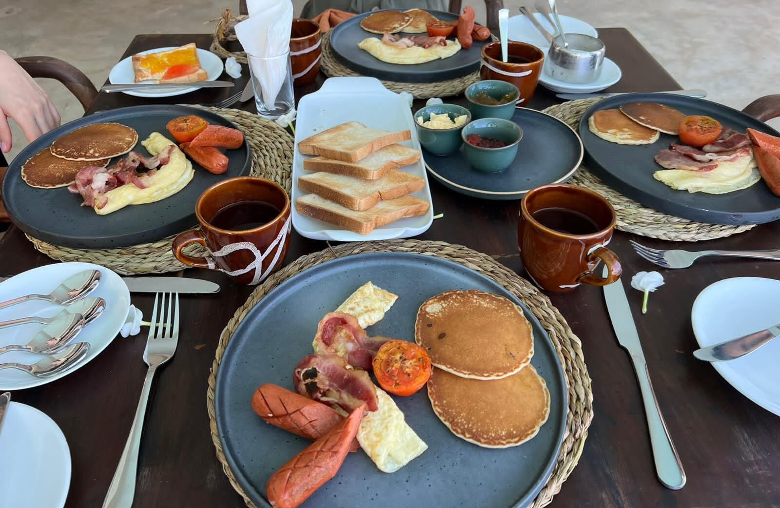 A breakfast buffet with pancakes, bacon, eggs, toast, and various spreads.