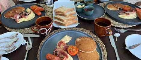 A breakfast buffet with pancakes, bacon, eggs, toast, and various spreads.