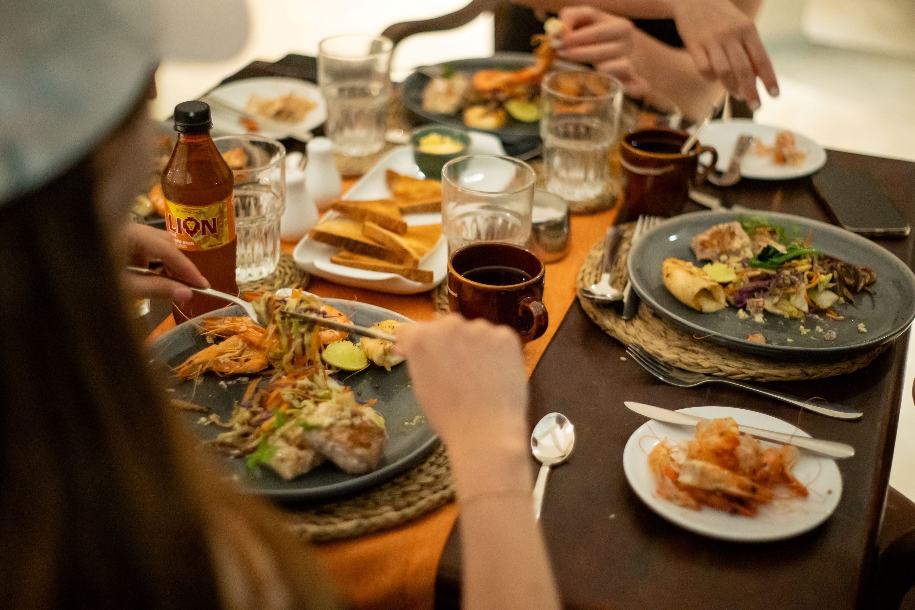 A dining table with various dishes, including shrimp and vegetables, and a bottle of sauce.