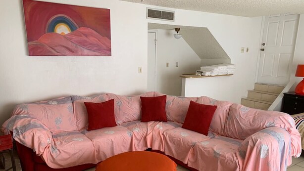 A living room with a pink sofa, red cushions, a red ottoman, a painting on the wall, and a staircase in the background. - Central, 3 bed-rooms, 2 showers, 5 mins airport, 10 mins strip/convention center (Las Vegas)