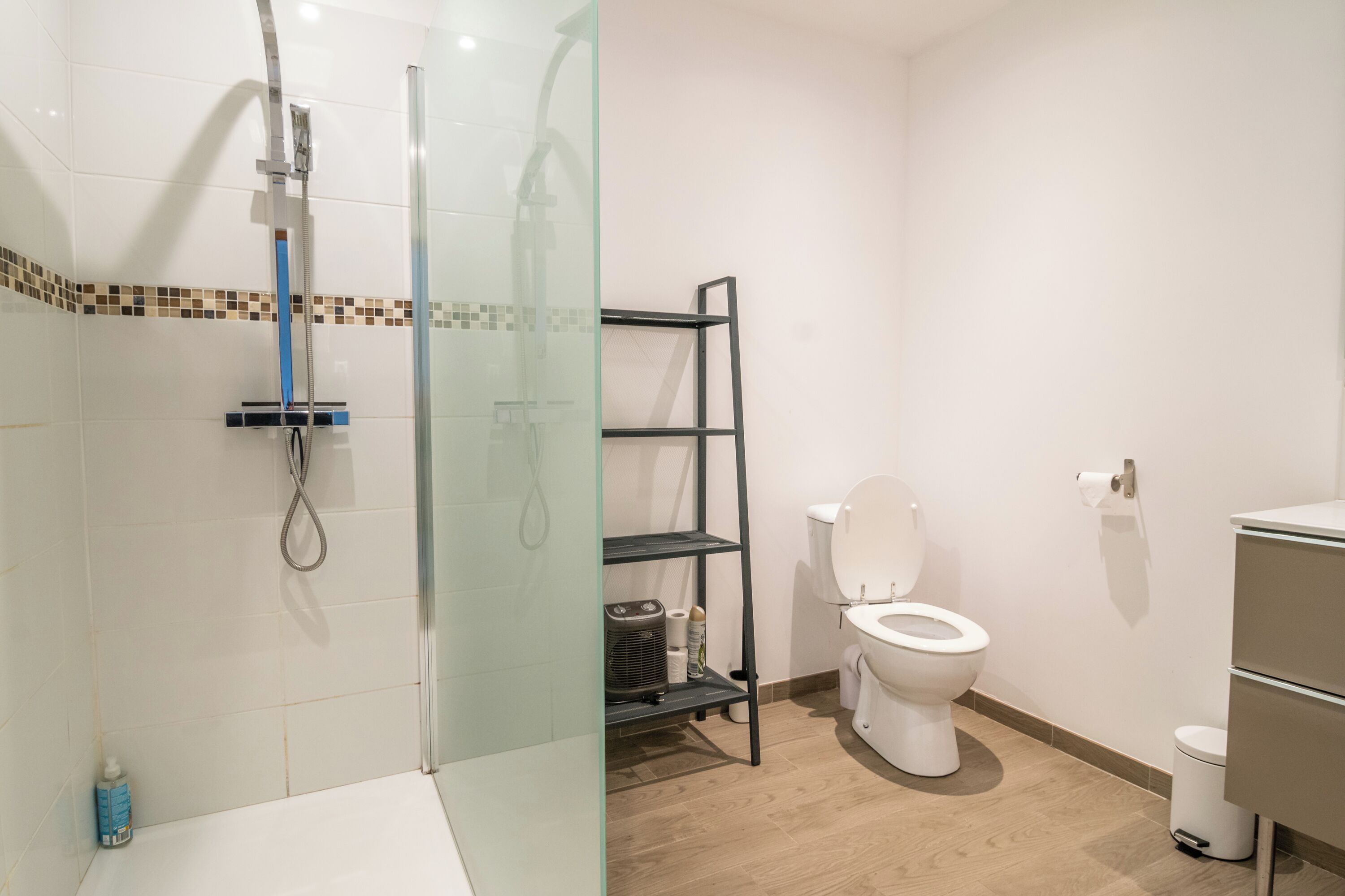 A modern bathroom with a glass-enclosed shower, a white toilet, and a black shelf unit.