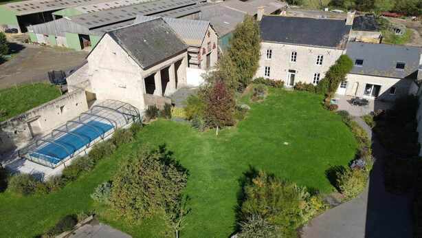 Eine Vogelperspektive zeigt ein Anwesen mit Schwimmbad, großem Rasen und einem Gebäude in markanter Architektur.