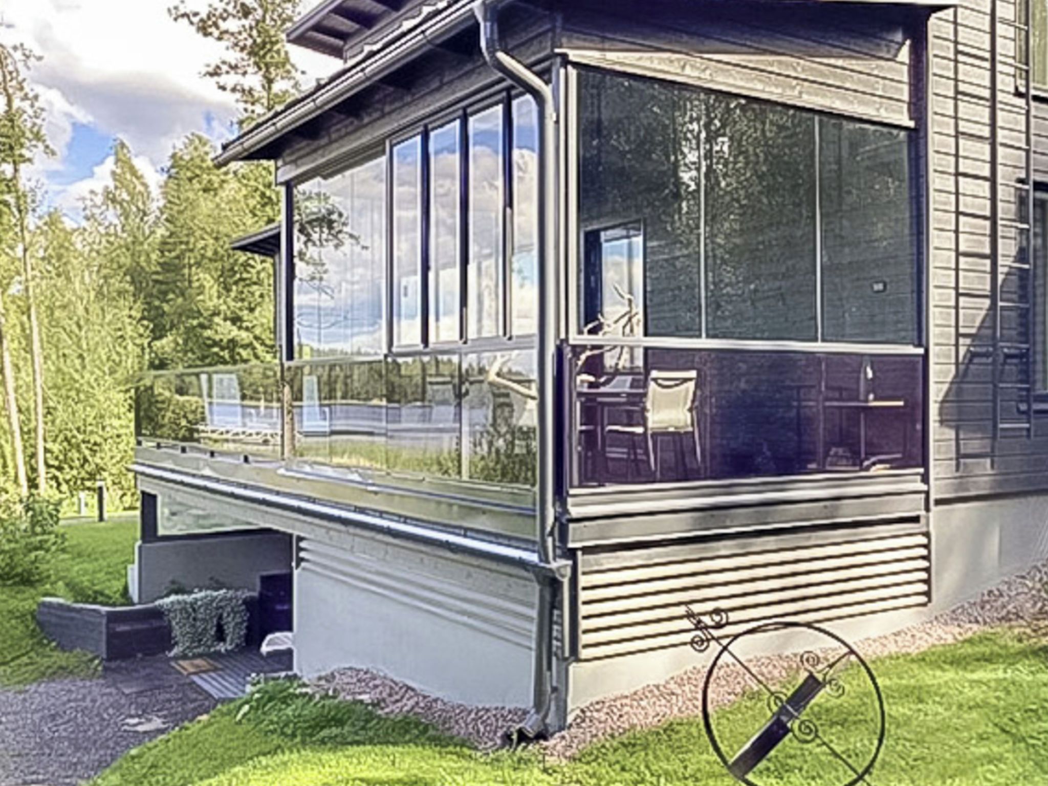 A modern house with a large glass window, a covered porch, and a view of a lake.