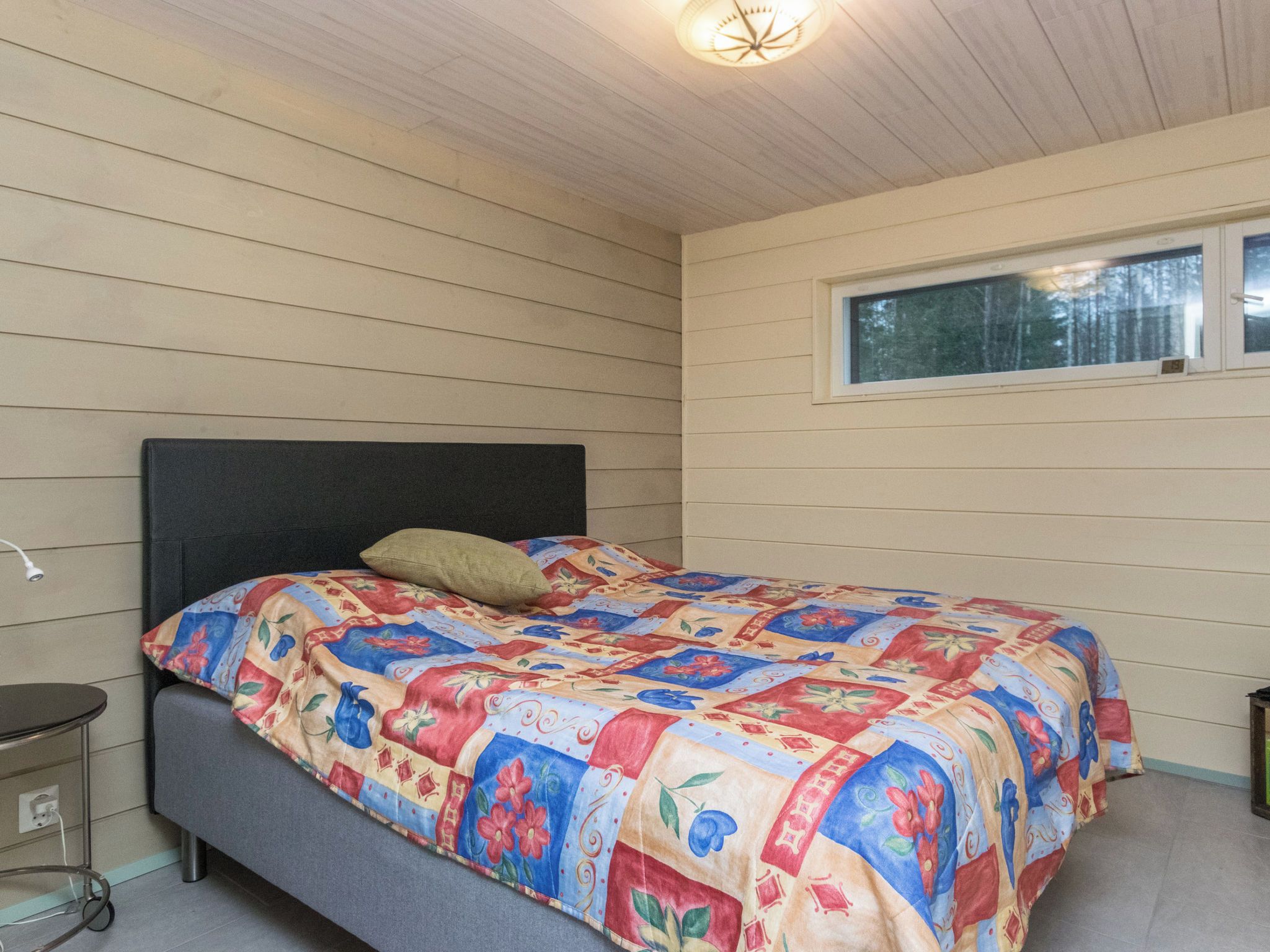 A bedroom with a bed, a window, and a bedside table.