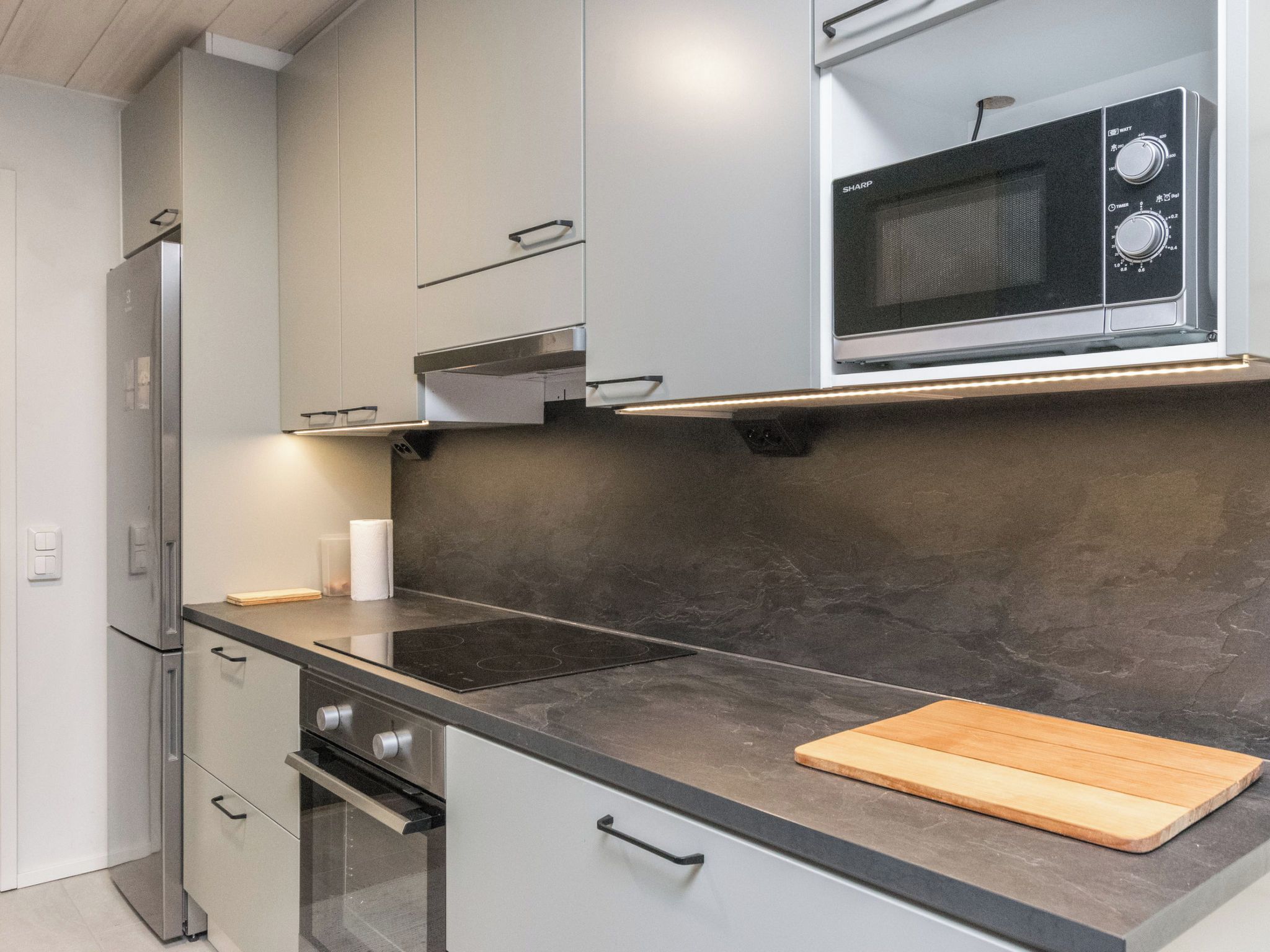 A modern kitchen with a built-in microwave, a stainless steel refrigerator, and a black countertop.