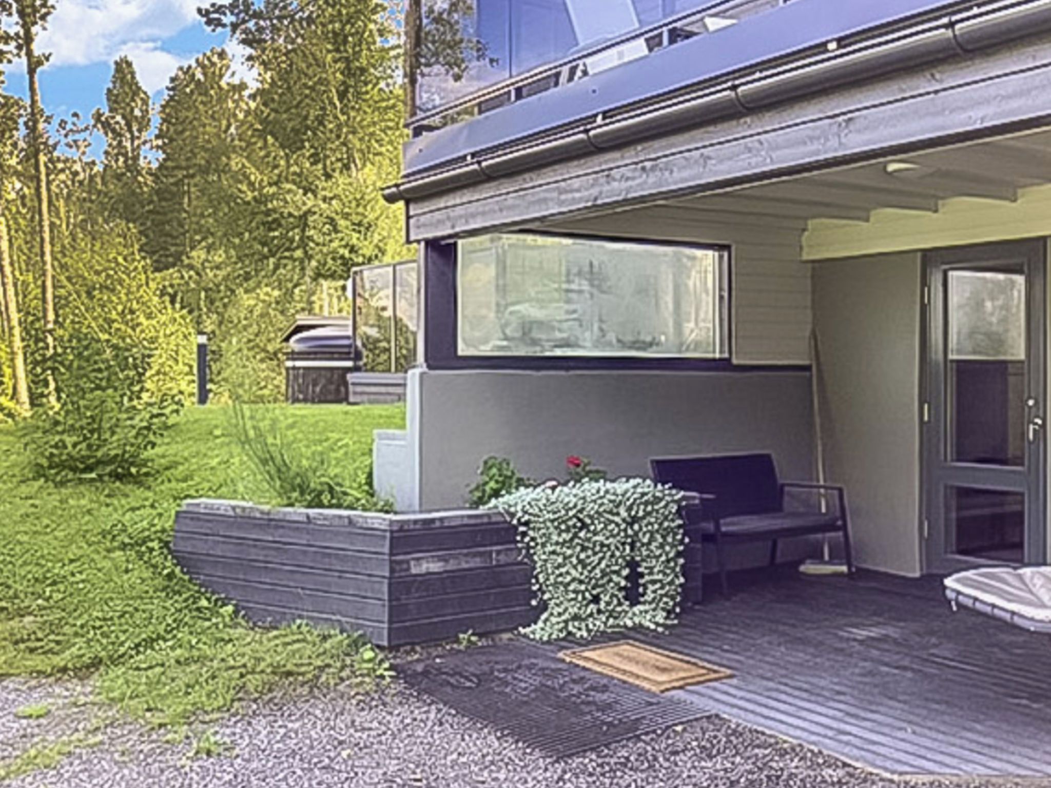 A modern house with a deck, a bench, and a window overlooking a garden.