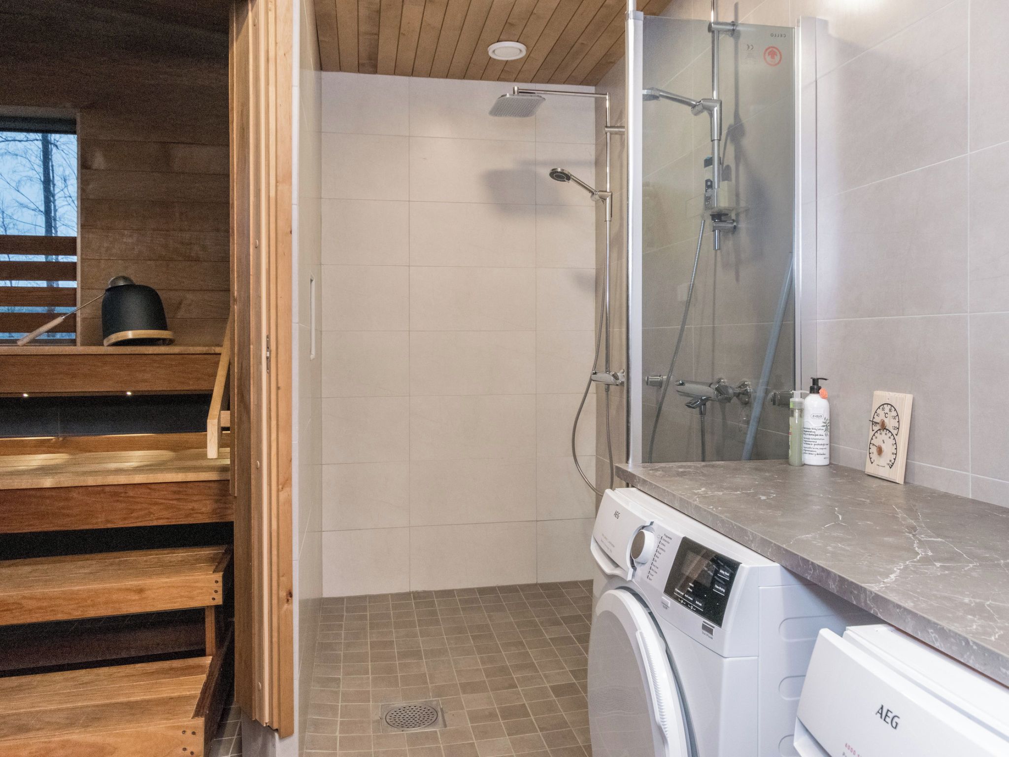 Une salle de bain moderne équipée d’une douche, d’un lave-linge et d’un banc en bois.