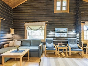 A log cabin interior with a sofa, armchairs, a small table, and a painting on the wall.