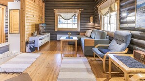 A log cabin interior with a wooden floor, a sofa, a chair, a small table, and a television.