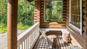 A log cabin with a wooden deck, a bench, and a table.