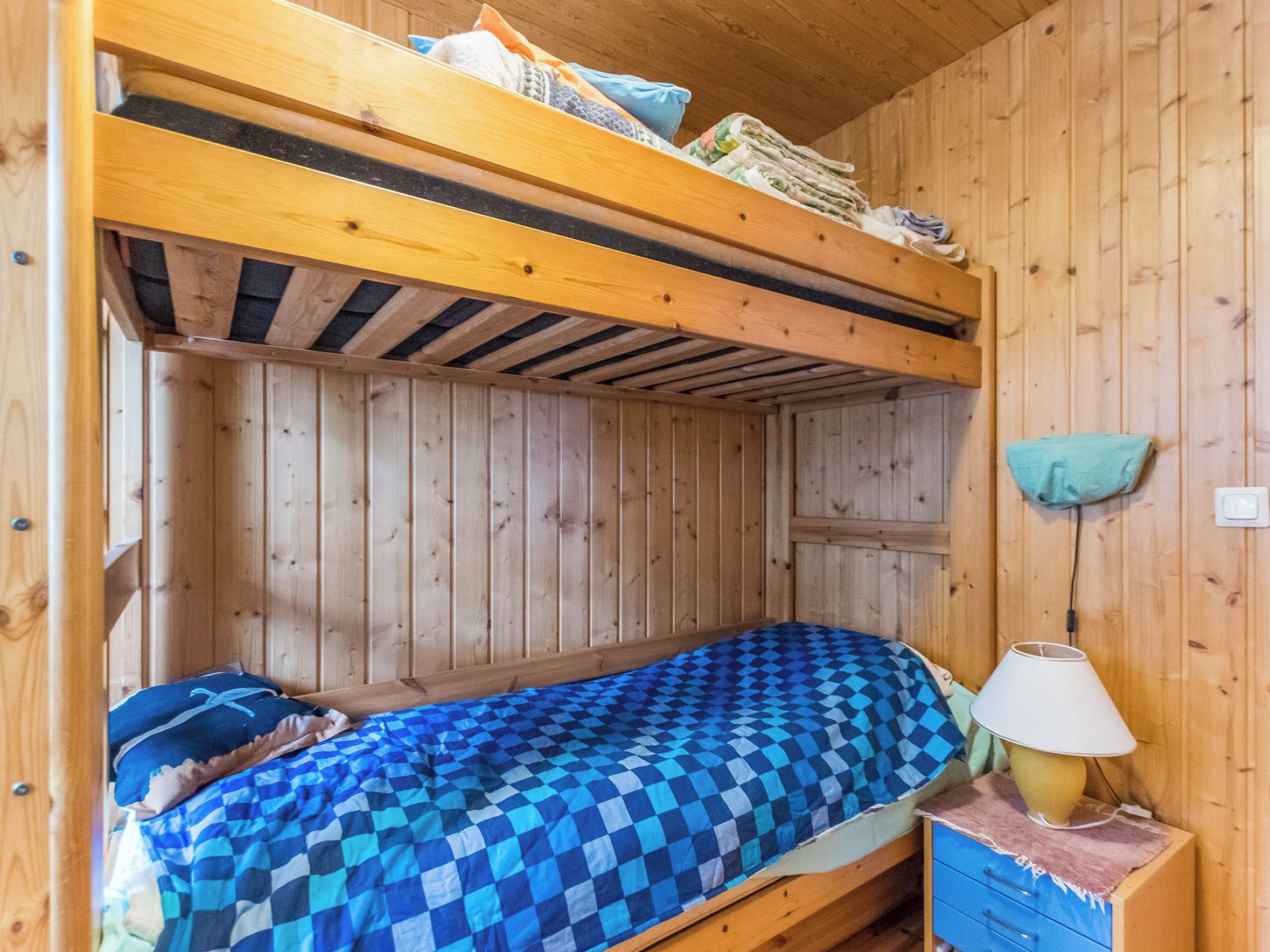 A bunk bed with a checkered blanket, a bedside lamp, and a small drawer unit.