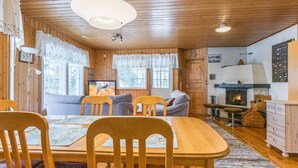 L’intérieur chaleureux d’un chalet avec une table à manger, des chaises, un canapé, une cheminée et des murs en bois.