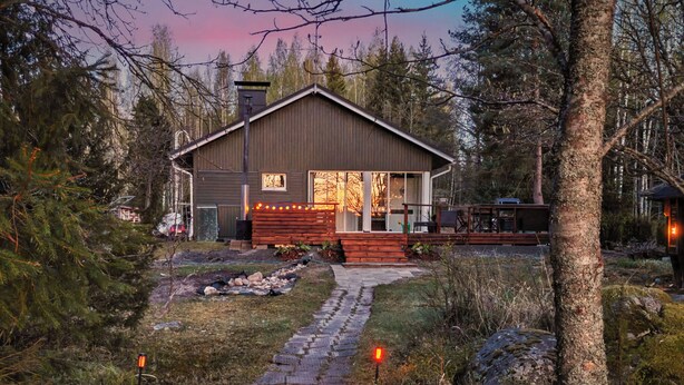 Un chalet rustique doté d’une terrasse en bois, d’un chemin de pierre menant à l’entrée et surplombant une forêt.