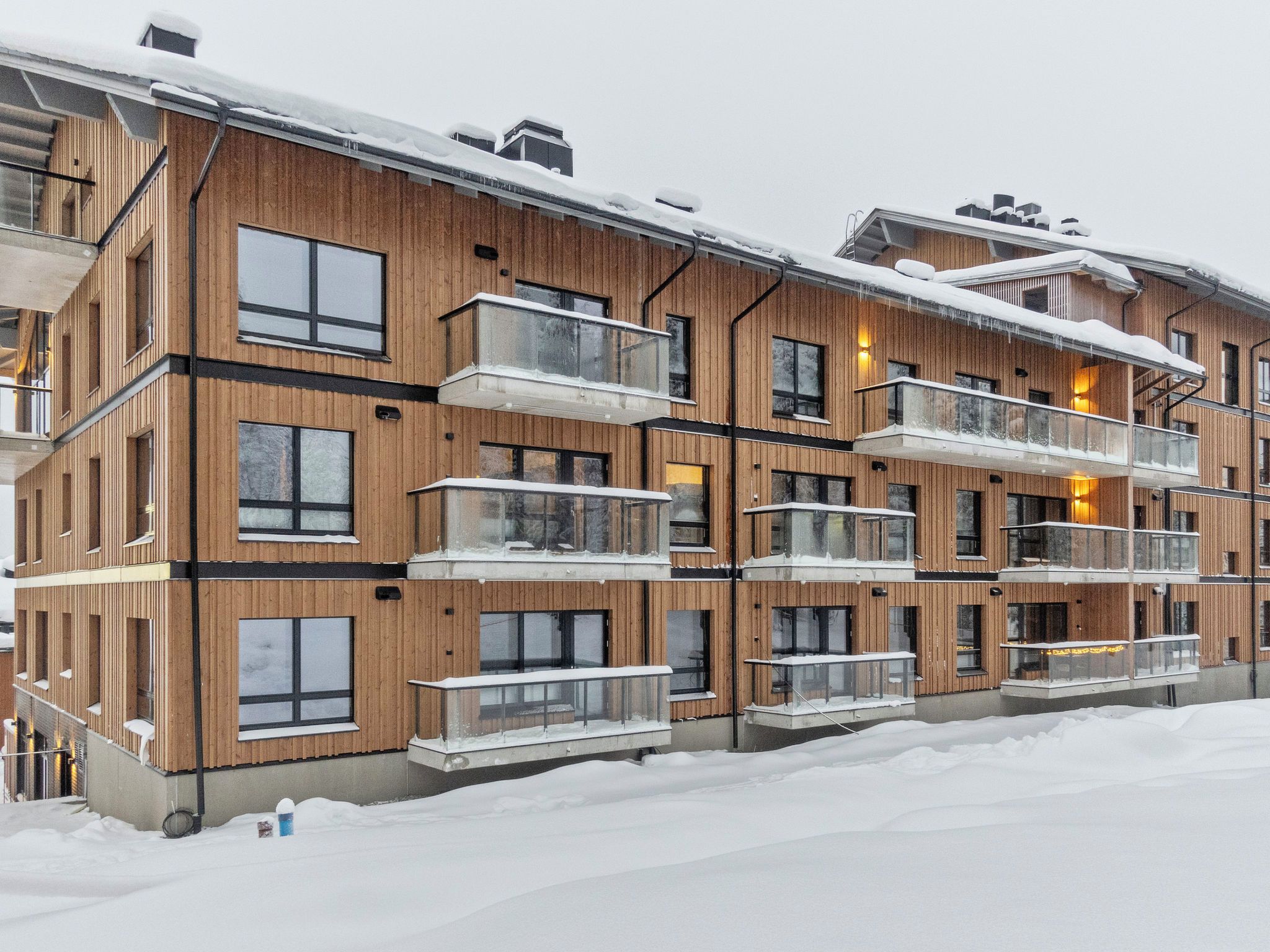 Een meerlaags houten gebouw met balkons en grote ramen, omgeven door sneeuw.