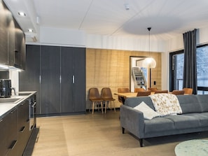 A modern kitchen with dark cabinets, a dining area with a wooden table and chairs, and a gray sofa with a throw blanket.
