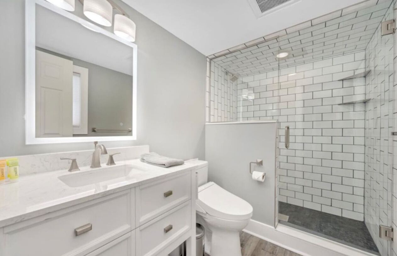 A modern bathroom with a white vanity, a large mirror, a toilet, and a glass-enclosed shower area.
