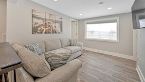 Un salon moderne avec un canapé gris, un tableau au mur et une grande fenêtre.