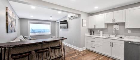 A modern kitchen with a bar area, white cabinets, and a wooden floor.