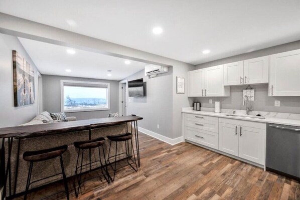 A modern kitchen with a bar area, white cabinets, and a wooden floor.