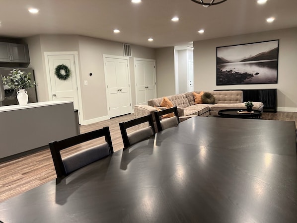 Una sala de estar moderna con una gran mesa de comedor, un sofá y una zona de cocina con armarios y un refrigerador.