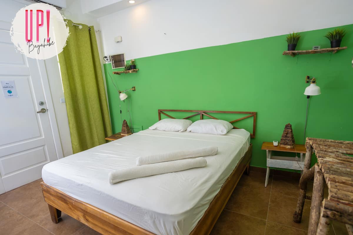 A neatly made bed with white linens and a wooden headboard in a room with green walls and brown tiled flooring.