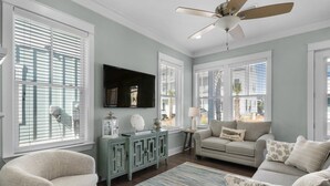 A living room with a ceiling fan, a flat-screen TV, and a sofa.