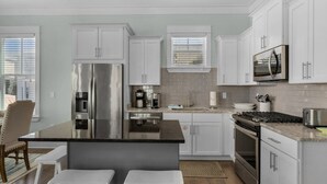 A modern kitchen with white cabinetry, stainless steel appliances, a central island with stools, and a view of the outdoors through large windows.