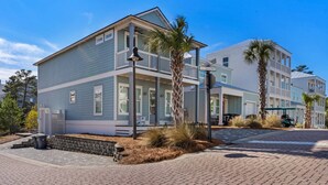 A coastal residential building with a balcony, a covered porch, and a driveway.