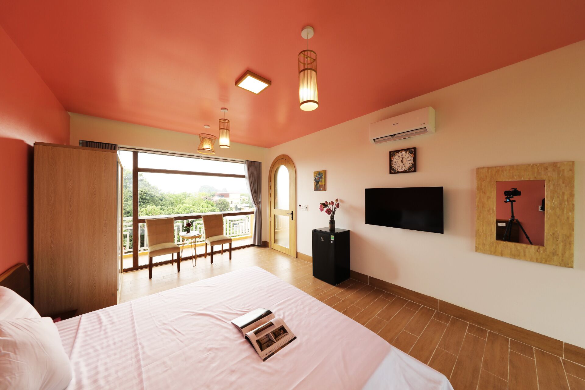 A bedroom with a large bed, a TV, a clock, and a balcony with a view.