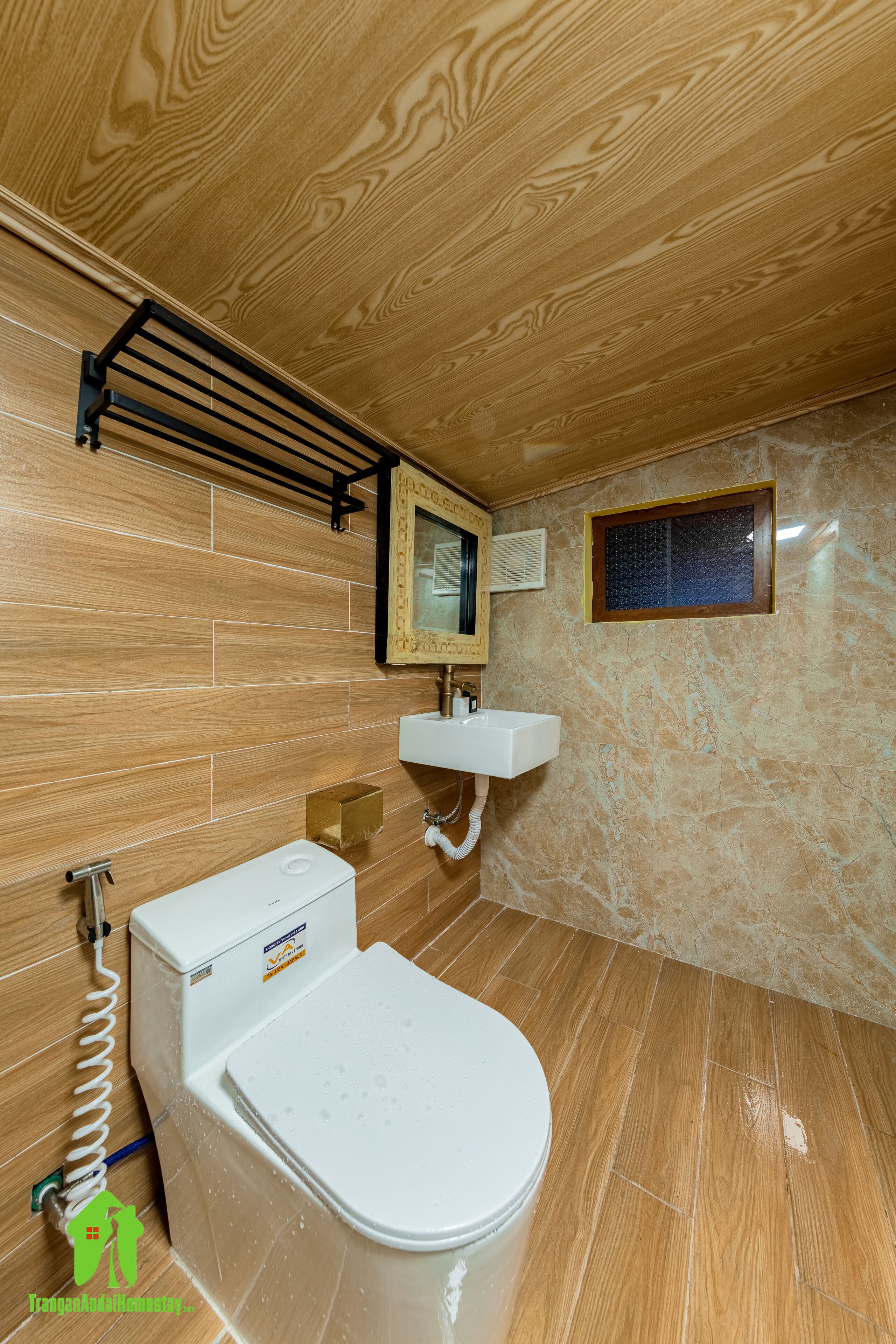 Ein Badezimmer mit Holzboden, Toilette in Weiß, einem Waschbecken und einem Handtuchhalter.