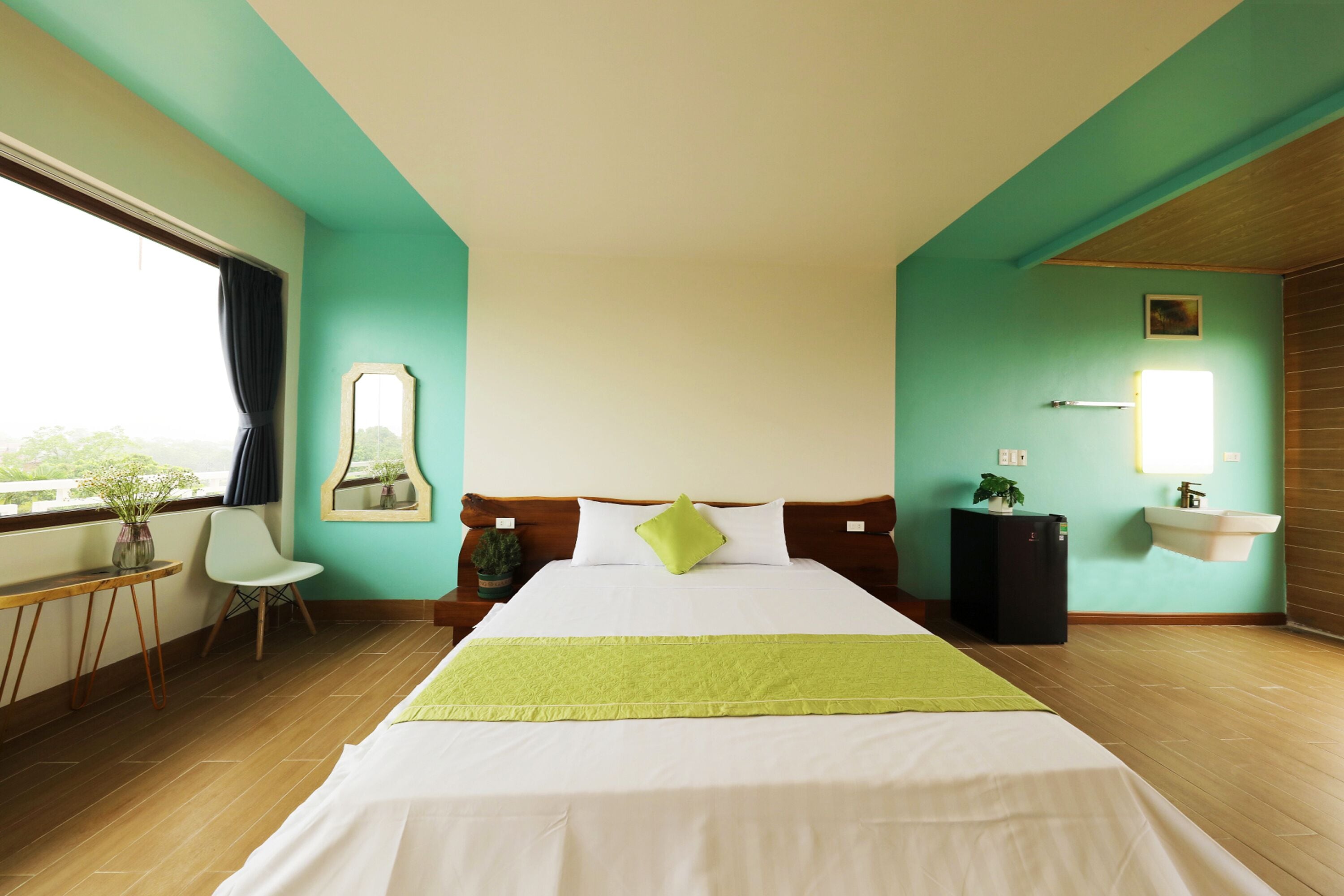 Ein Hotelzimmer mit Bett, Schreibtisch, Stuhl, einem fenster mit Vorhängen, Spiegel, Waschbecken und einer Topfpflanze.