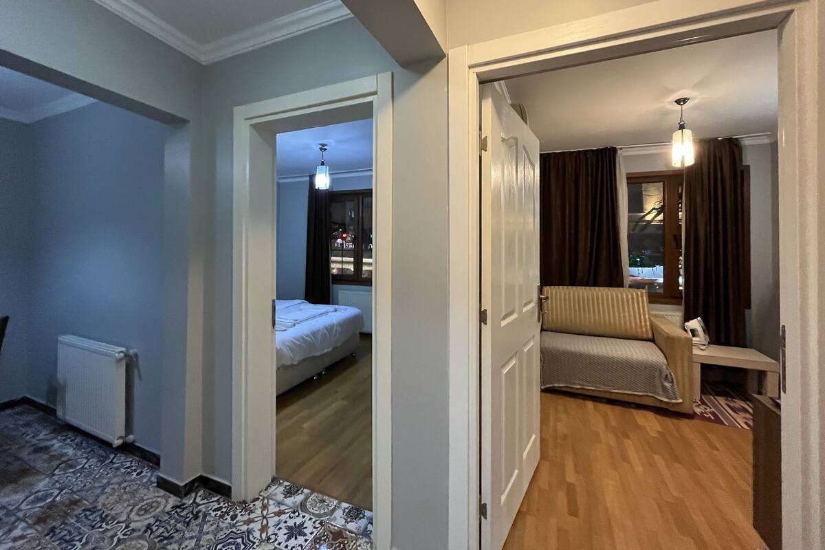 A hotel room with a bed, a chair, a radiator, and a window with curtains.