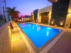 Piscina rectangular con plataforma de azulejos, rodeada de muros de piedra y plantas en macetas.
