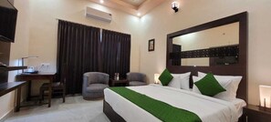 Habitación de hotel con cama, escritorio, dos sillas, televisor y un espejo grande.