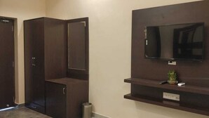 A room with a dark wooden wardrobe, a mounted TV on the wall, and a small shelf below it.